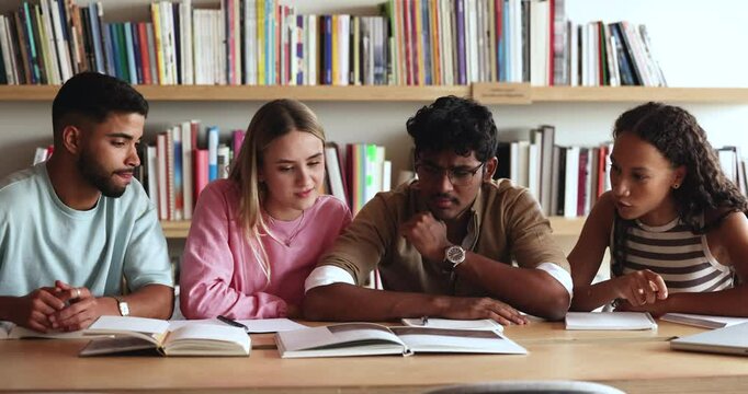Diverse team of focused young students studying textbook in library together, watching picture, pointing at page, talking, discussing article, text, preparing group report for class, doing research