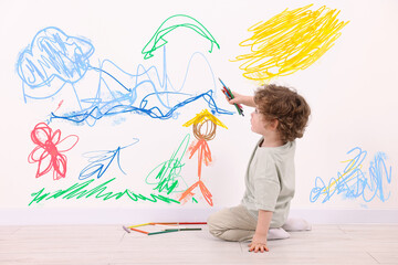 Little child sitting on floor and drawing on white wall