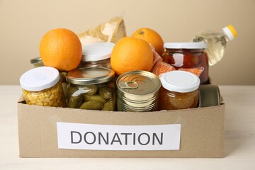 Different food products for donation in box on table against beige background