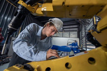 Engineer standing by robotic arm and operating machine in industry factory, technician worker check for repair maintenance electronic operation