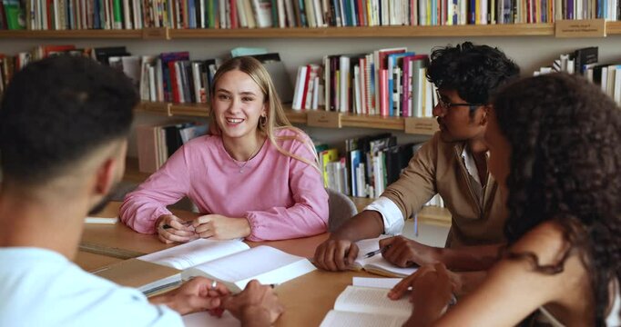 Positive young Caucasian student girl talking to diverse group of classmates in library, discussing learning project, telling self presentation to new multiethnic university friends
