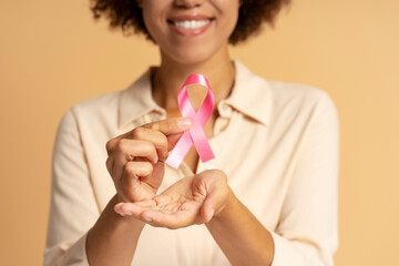 Smiling young woman holding pink ribbon for breast cancer awareness