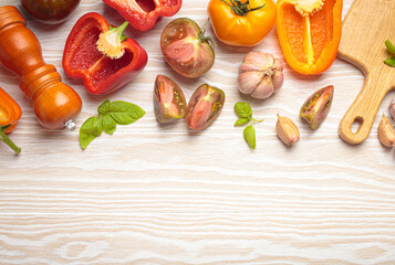 Colorful vegetables, a pepper mill, and a cutting board are filling the top of a white wooden tabletop frame. The arrangement leaves an empty space on the bottom for text or design