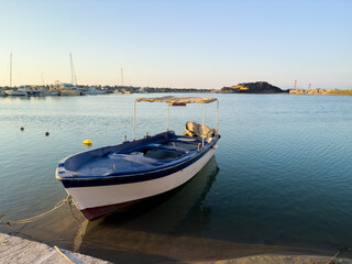 A Tranquil Fishing Boat Rests in Calm Waters During Sunset Near a Serene Coastal Harbor