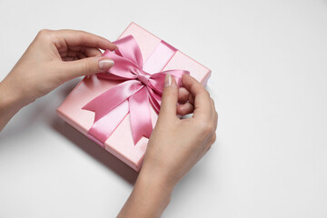 Woman decorating gift box with bow on white background, closeup