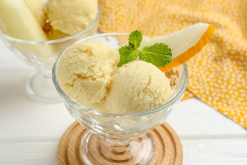 Scoops of melon sorbet with mint and fresh fruit in glass dessert bowls on white wooden table, closeup