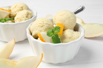 Scoops of melon sorbet with mint and fresh fruit in bowls on white wooden table, closeup