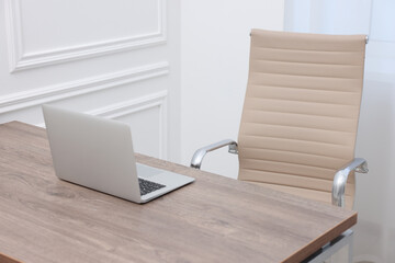 Beige leather chair, laptop and desk in office