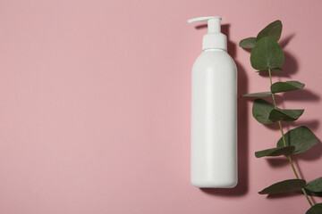 Bottle of shampoo and eucalyptus branch on pink background, flat lay. Space for text