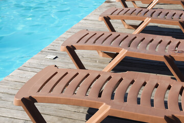 Empty sun loungers on wooden deck near outdoor swimming pool, closeup
