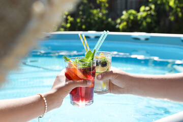 Women holding tasty cocktail in glass near swimming pool outdoors, closeup