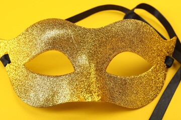 One golden carnival mask on yellow background, closeup