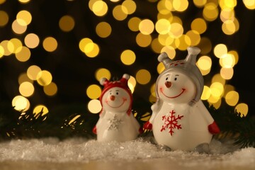 Cute decorative snowmen on artificial snow against blurred lights. Space for text