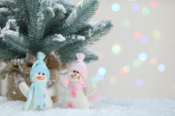 Cute snowmen and fir branches against beige background with blurred lights, bokeh effect. Space for text