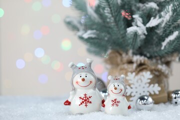 Cute snowmen, Christmas balls and fir branches against beige background with blurred lights, bokeh effect