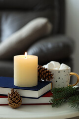 Burning candle, books, fir branches and cones on coffee table indoors, space for text. Christmas atmosphere