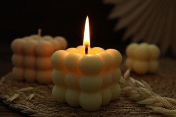 Burning bubble candle on wicker mat against black background, closeup