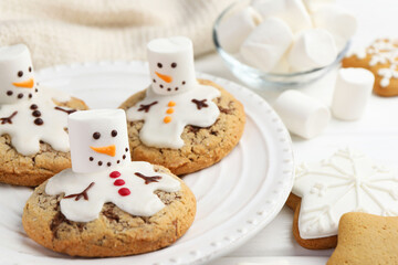 Delicious cookies with snowmen made of marshmallows on white table, closeup
