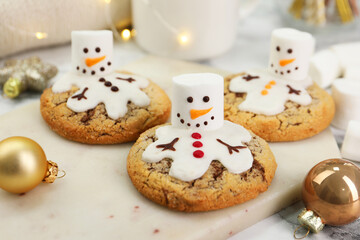 Delicious cookies with snowmen made of marshmallows on white table, closeup