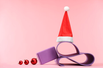 Yoga mat, Santa hat and baubles on pink background, space for text