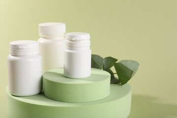 Plastic medical bottles, leaves and podiums on green background, closeup