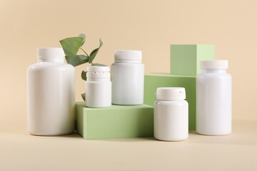 Plastic medical bottles, eucalyptus leaves and podiums on beige background
