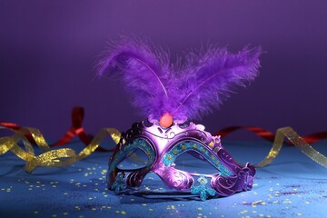 Beautiful bright carnival mask, ribbons and confetti on color background