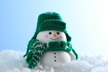 Cute decorative snowman on artificial snow against light blue background, closeup