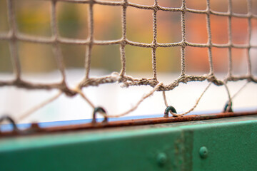 sports net secured to a fence using metal eyelets, illustrating its functionality and connection to athletic activities. The setup emphasizes safety and organization in sports environments