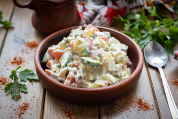 Olivier salad in a plate on a wooden table. Salad with peas, ham and mayonnaise. Salad with meat and vegetables on a wooden background. Close-up