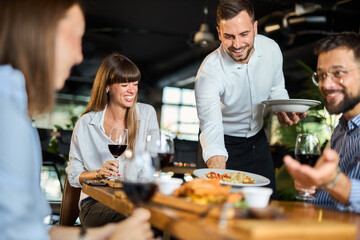 Mid adult waiter serving group of business people during lunch time in a restaurant.