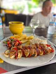 Delicious plate of grilled chicken skewers with rice, salad, and fries on a wooden table setting. Well-balanced and colorful meal, perfect for a vibrant dining experience