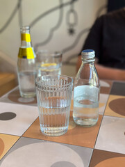 Glass of water alongside a bottle on a patterned tile table. Depicting everyday hydration and minimalistic lifestyle themes.