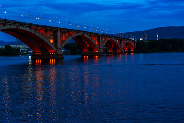 Illuminated bridge over river at dusk with reflections on wate