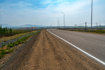 Paved road with dirt shoulder in rural landscape and distant mountains