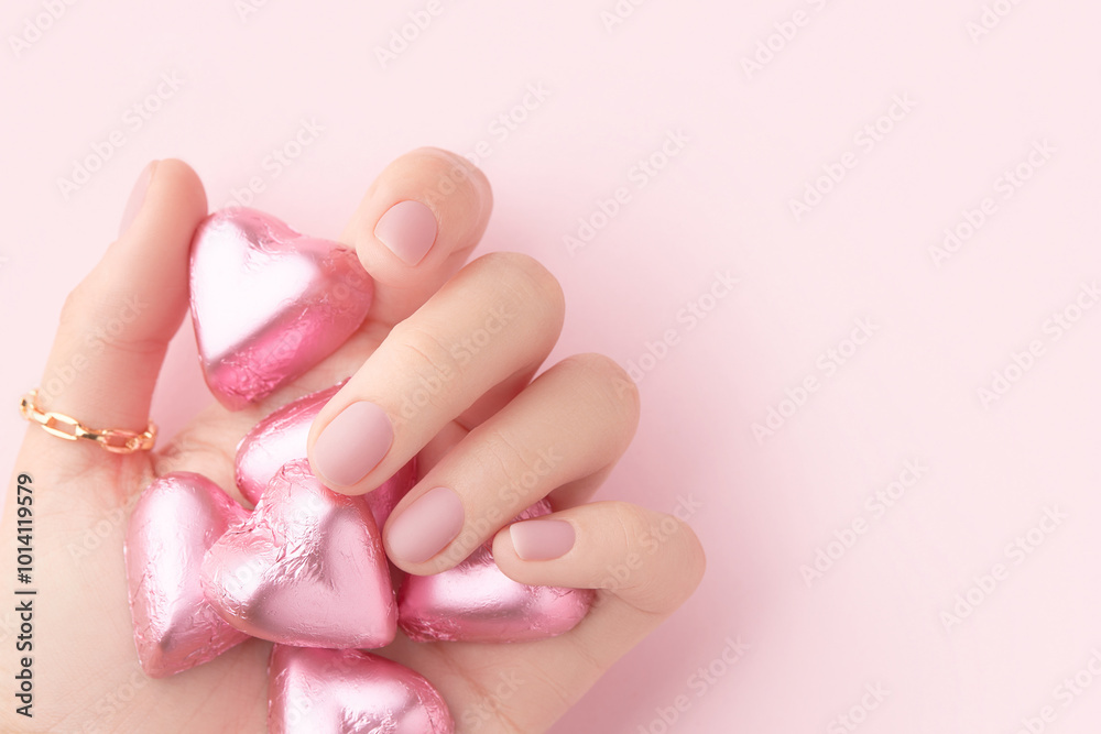 Sticker womans hand with trendy pink matte manicure holding candy close-up