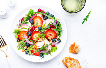 Foodie food salad with strawberry, grilled chicken, arugula, blueberries and walnuts with ciabatta, white table., top view