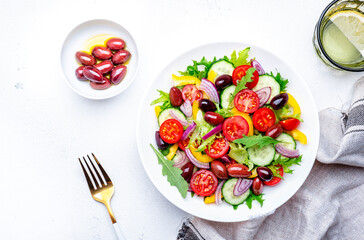 Colorful vegetable salad with olives, tomato, paprika, cucumber, onion, and herbs. White background, top view