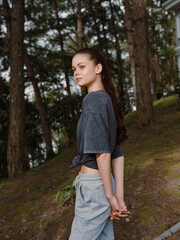 Young woman standing outdoors in casual attire, gazing over her shoulder, showcasing a relaxed demeanor in a natural setting surrounded by greenery