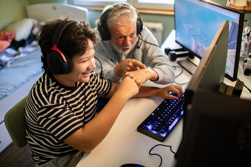 Grandfather and grandson playing video games together on PC with headsets