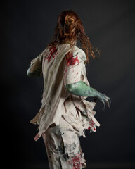 Fototapeta premium Close up portrait of scary female model wearing spooky halloween costume wearing, ripped clothes and fake blood like an undead apocalyptic zombie character. Isolated figure on dark studio background