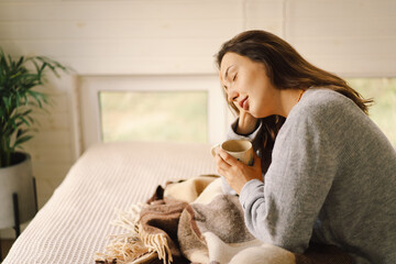 A woman relaxes in a bright, serene room, sipping coffee while focused on her book. The natural...