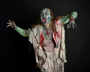 Close up portrait of scary female model wearing spooky halloween costume wearing, ripped clothes and fake blood like an undead apocalyptic zombie character. Isolated figure on dark studio background