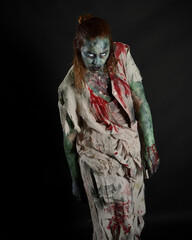 Close up portrait of scary female model wearing spooky halloween costume wearing, ripped clothes and fake blood like an undead apocalyptic zombie character. Isolated figure on dark studio background