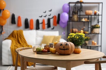 Halloween celebration. Pumpkin with creepy face, candles and flowers on wooden table in decorated room