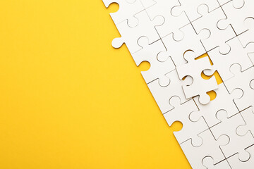 White puzzle pieces on yellow background, top view. Space for text