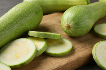 Board with fresh cut and whole zucchinis on table, closeup