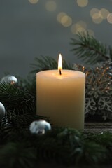 Burning candle, baubles and fir tree branches on wooden table, closeup