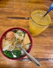 a bowl of meatball noodles with orange juice on a wooden table