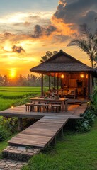 A small wooden bungalow with an open-air terrace, set in the middle of rice fields at sunset.